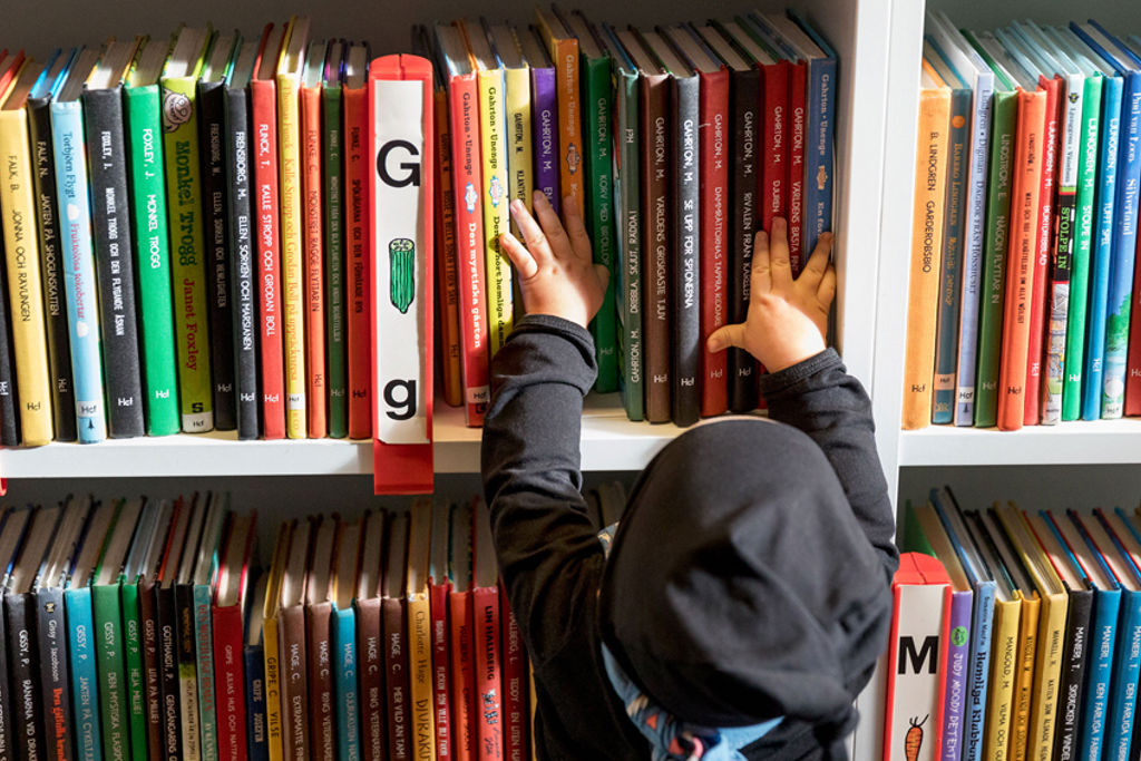Foto av ett litet barn som känner på böcker i bokhylla