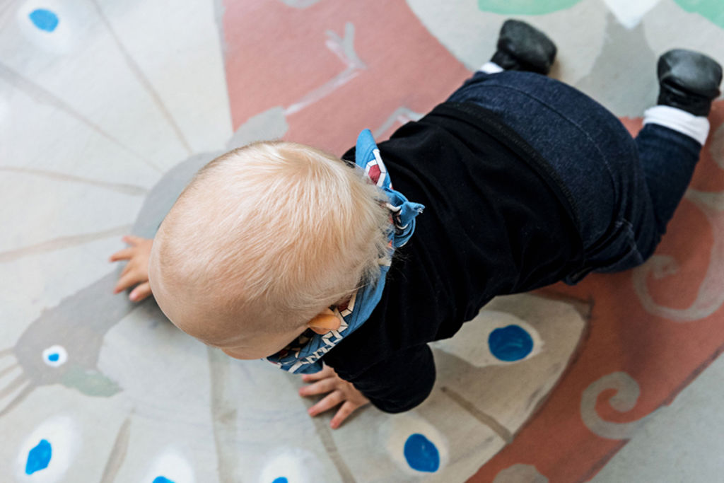 Fotografi av bebis som kryper över ett golv med en tecknad påfågel.