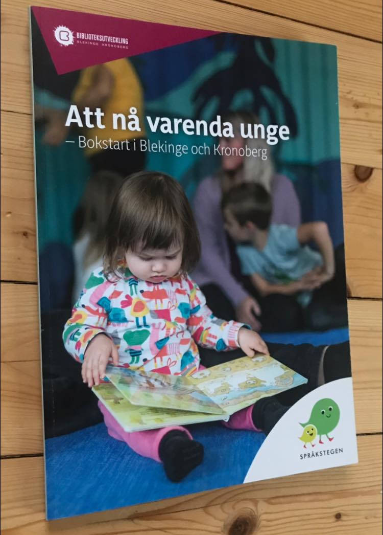 Skriften Att nå varenda unge - Bokstart i Blekinge och Kronoberg har ett läsande barn på omslaget och ligger på ett trägolv.