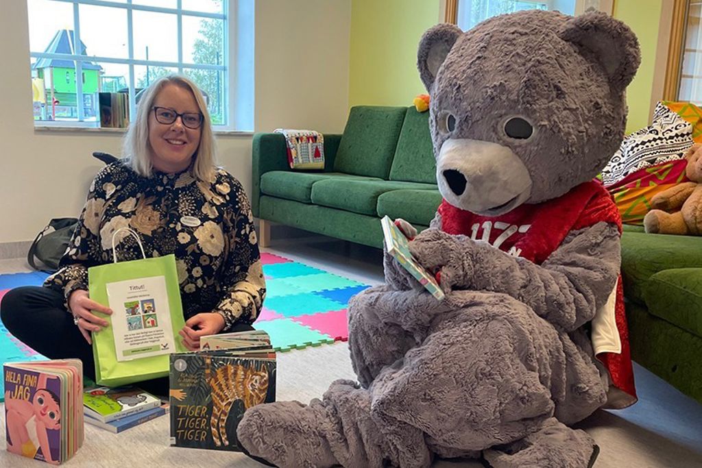 Kvinna och person i nalle-dräkt sitter på golvet framför en soffa.