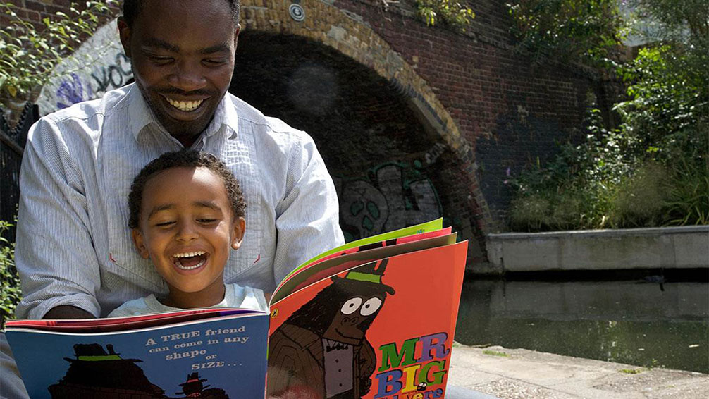 Foto av vuxen man och barn som läser bok tillsammans och skrattar