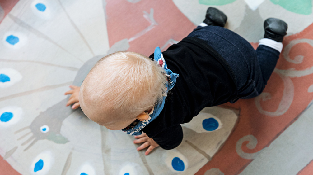 Foto av bebis som kryper på färgglad matta